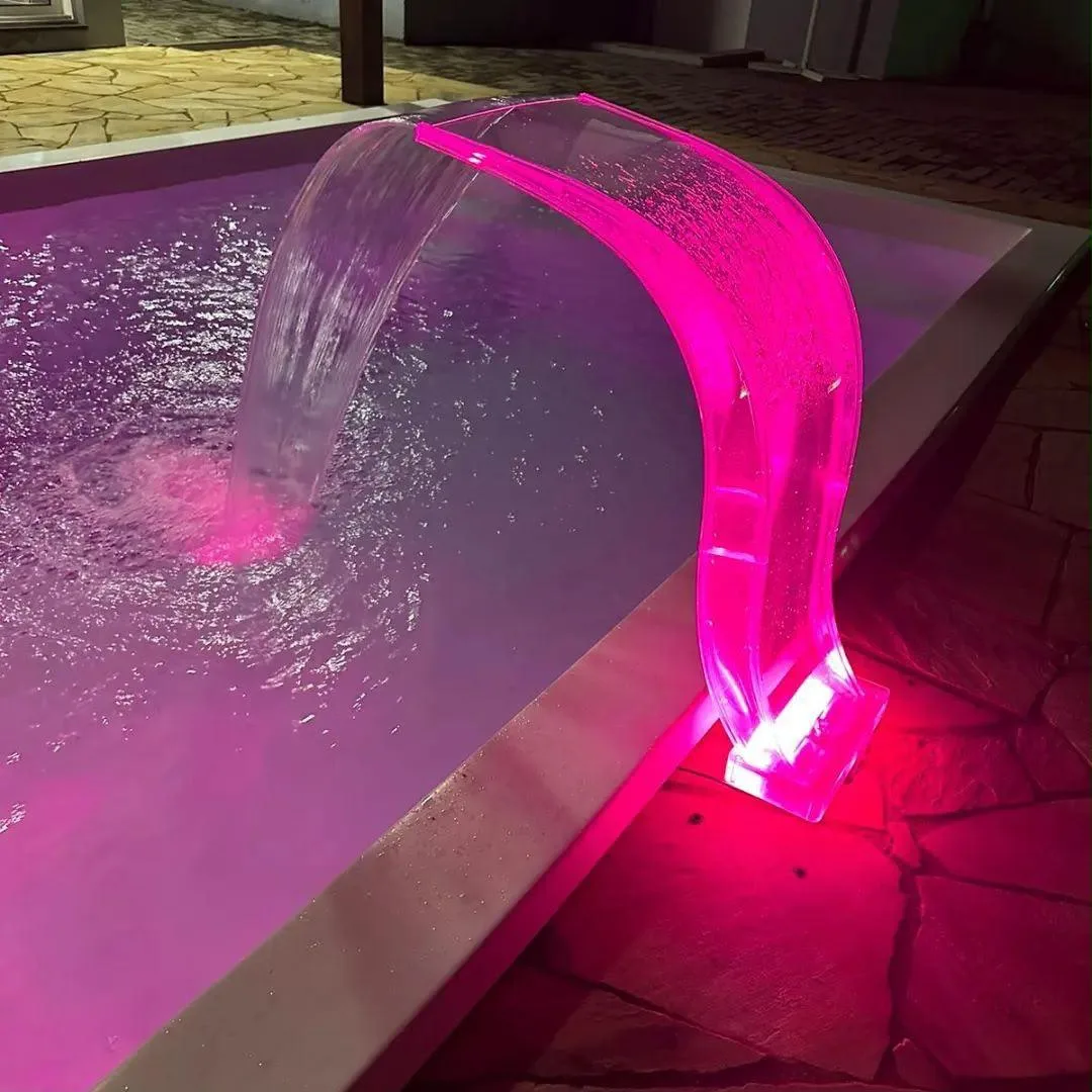 Detalhe de cascata transparente iluminada em rosa à beira da piscina