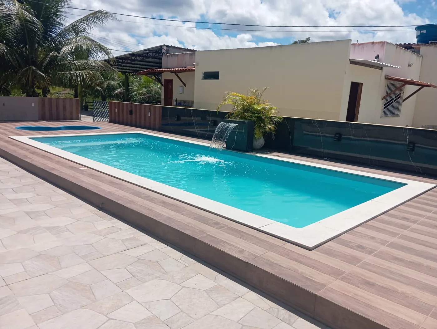 Piscina com borda branca e cascata em área externa ampla