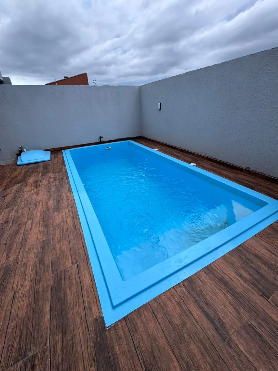 Piscina azul retangular instalada em pátio com piso amadeirado