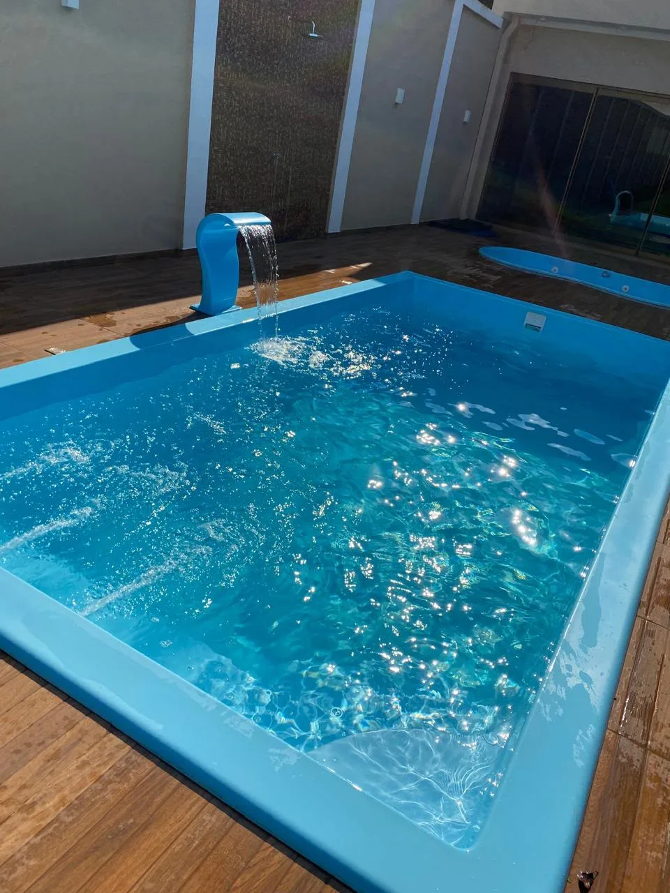 Piscina azul com cascata em funcionamento e deck ao redor