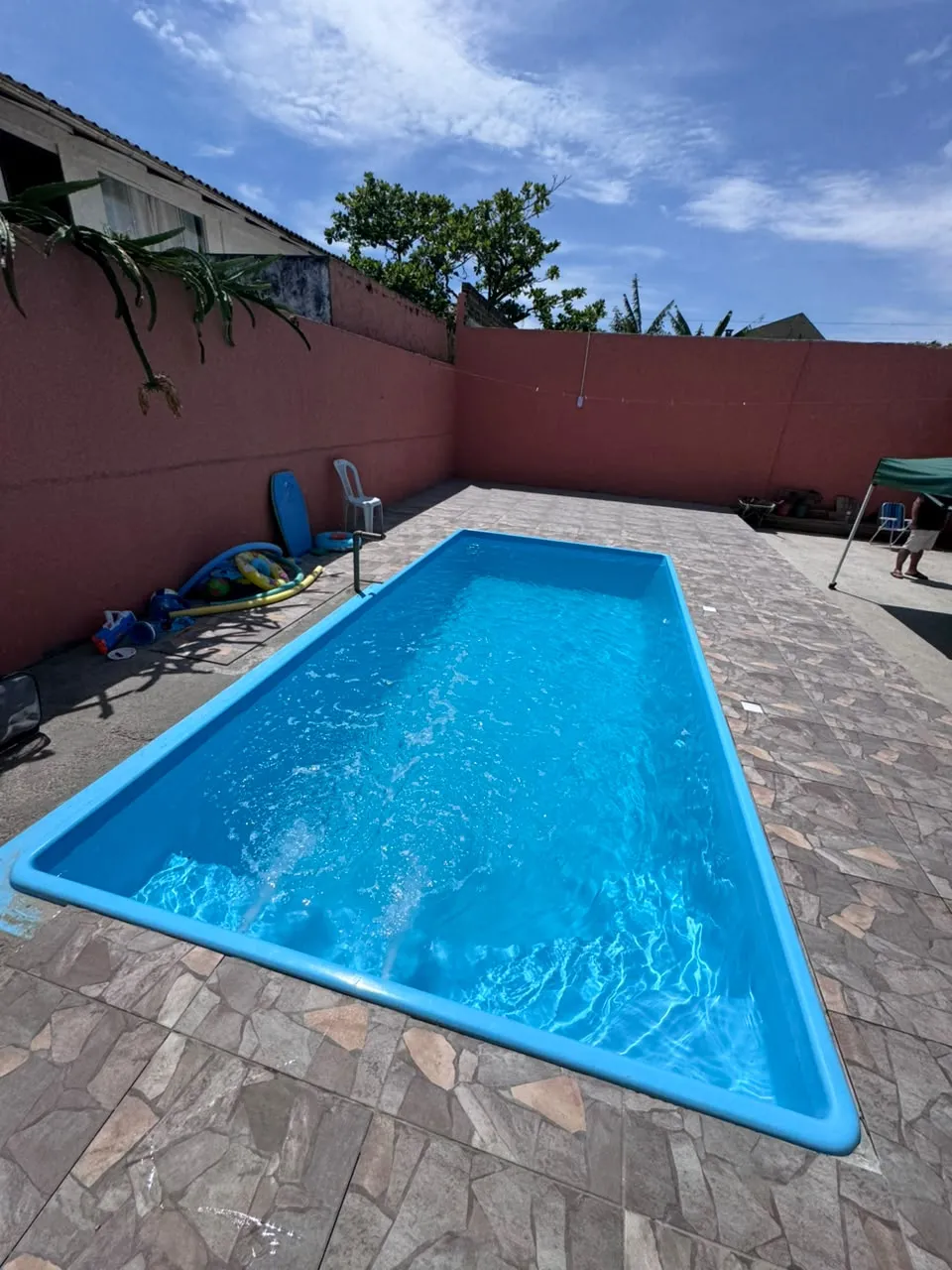 Piscina azul instalada em pátio com piso de pedra, em dia de sol